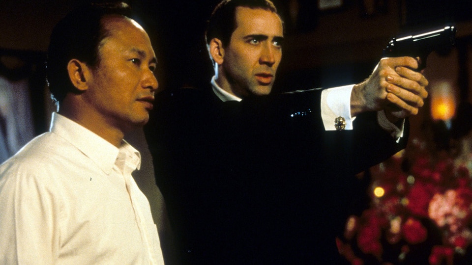 Director John Woo watches as Nicolas Cage aims pistol in between scenes from the film 'Face/Off' (1997)