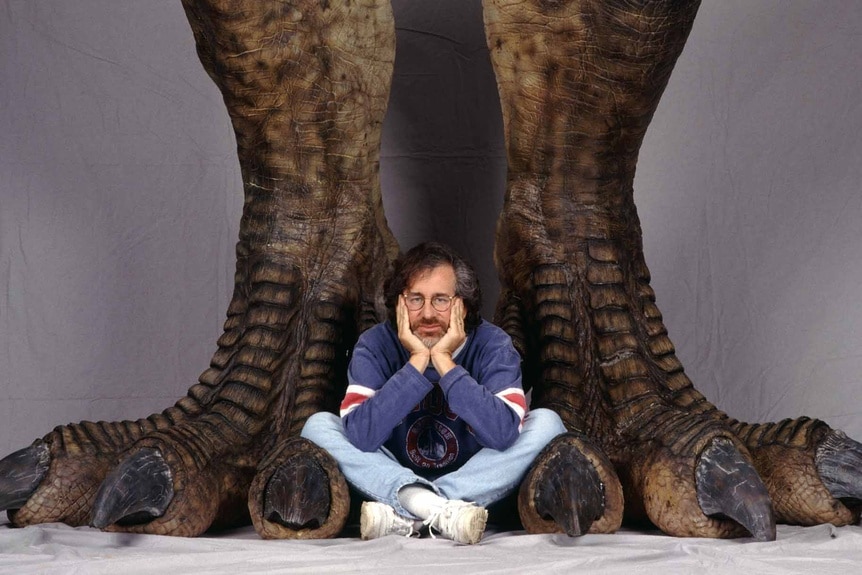 Steven Spielberg poses between a pair of giant dinosaur feet.