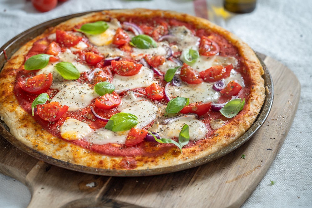 Pizza with mozzarella, tomatoes, onion, and basil.