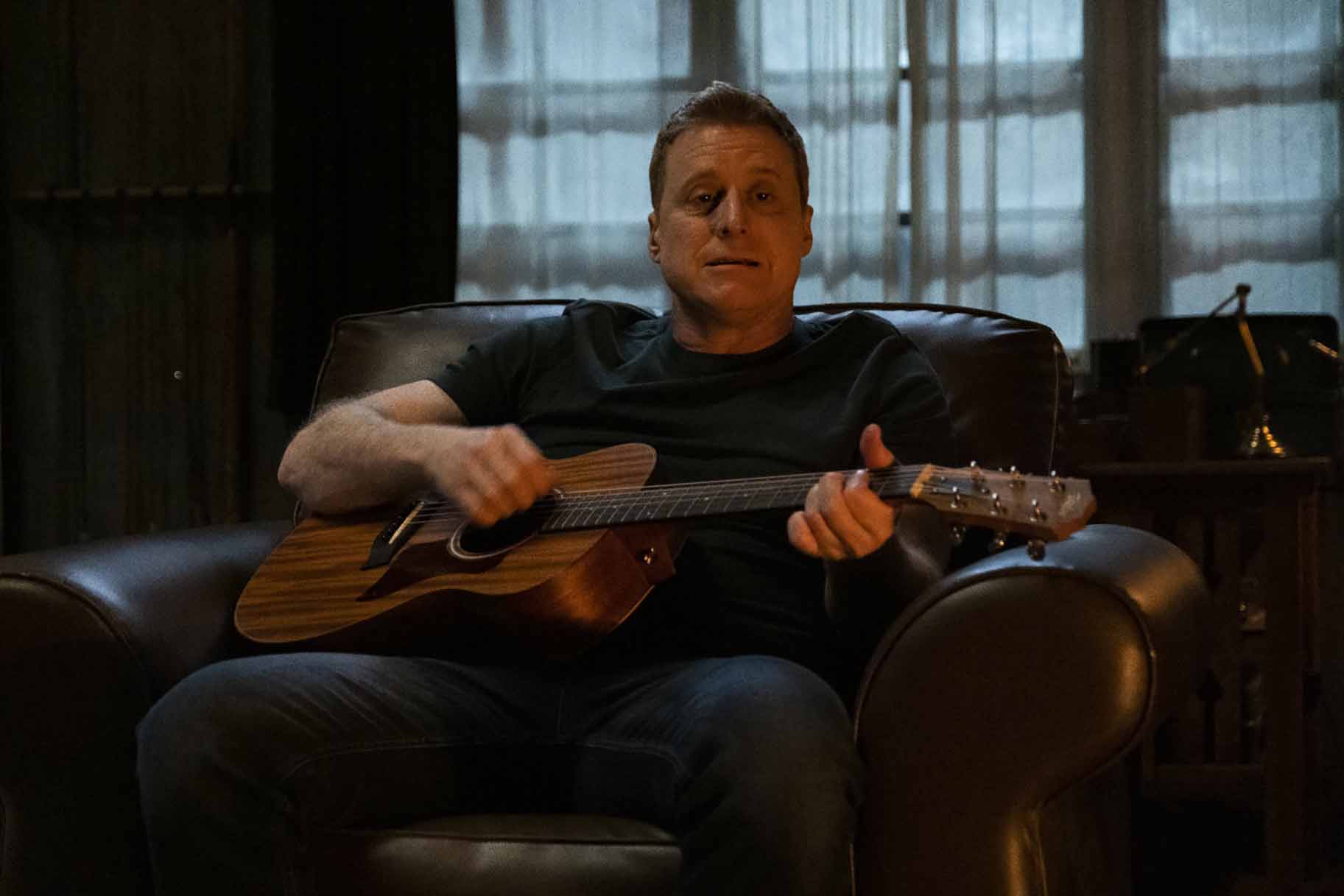 Harry Vanderspeigle (Alan Tudyk) sits while playing guitar in Resident Alien episode 306.