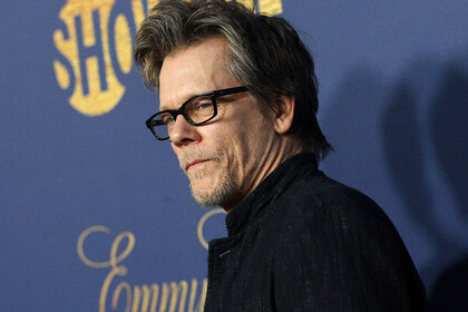 Kevin Bacon wears black glasses and poses.
