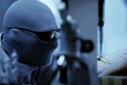 The Hollow Man injects a green liquid into an arm while fully covered in a morphsuit and sunglasses in Hollow Man 2 (2006).