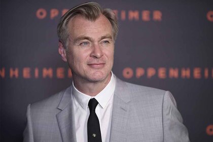 Christopher Nolan poses in a gray suit and black tie.