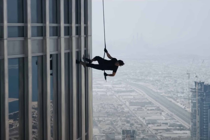 A cable-suspended Ethan Hunt (Tom Cruise) runs on the side of the building in Mission: Impossible – Ghost Protocol (2011).