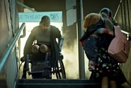 Fiona Dourif as Nica Pierce (Fiona Dourif) appears in a wheelchair at the top of the stairs as a little girl holding Chucky looks up at her in Chucky 303.