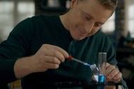 Harry drops blue liquid into a test tube in Resident Alien Episode 305.