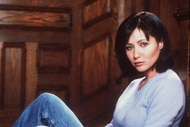 Shannen Doherty poses in jeans and a purple top.