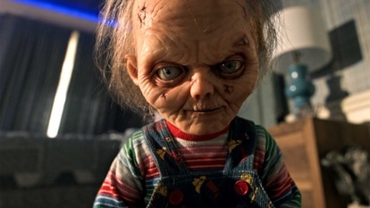 A close up of Chucky in a childs room looking beat up and old