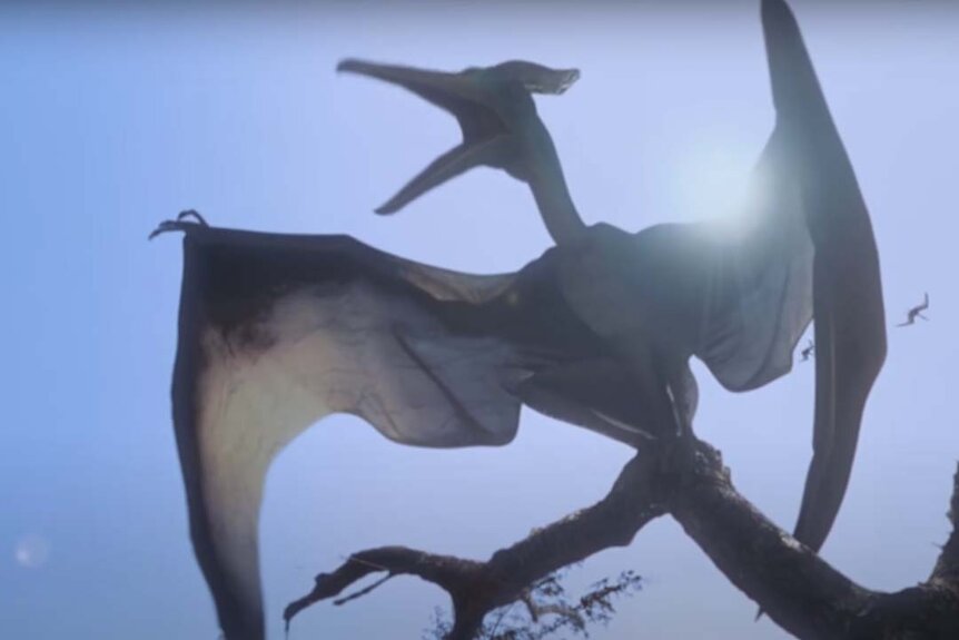 A backlit Pteranodon on a tree branch roars in the Jurassic Park film series.