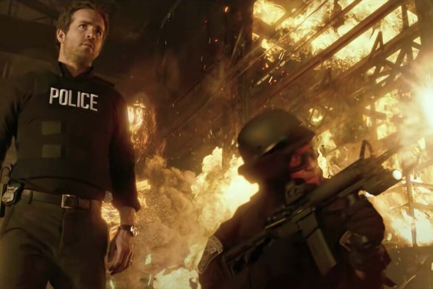 Nick Walker (Ryan Reynolds) walks past fiery combat in R.I.P.D. (2013)