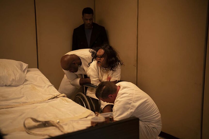 Victor Fielding (Leslie Odom, Jr.) watches as Angela Fielding (Lidya Jewett) wrestles with hospital attendants.