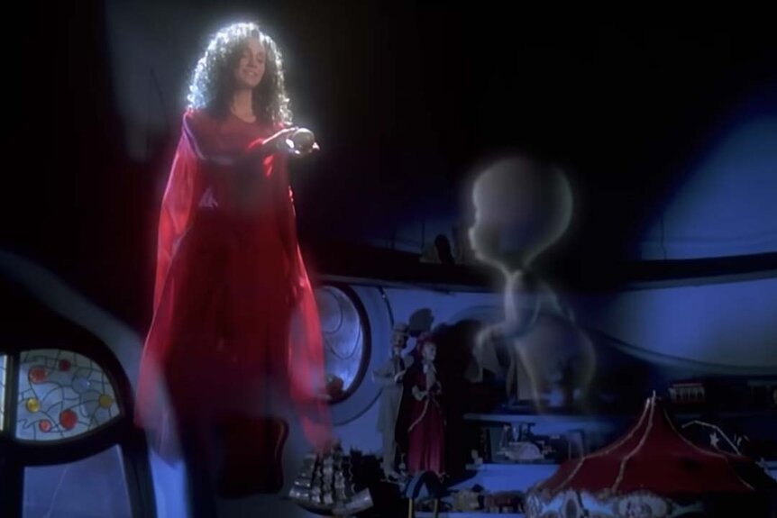 The glowing spirit of Amelia Harvey (Amy Brenneman) in a red dress hands a ball to Casper in Casper (1995).