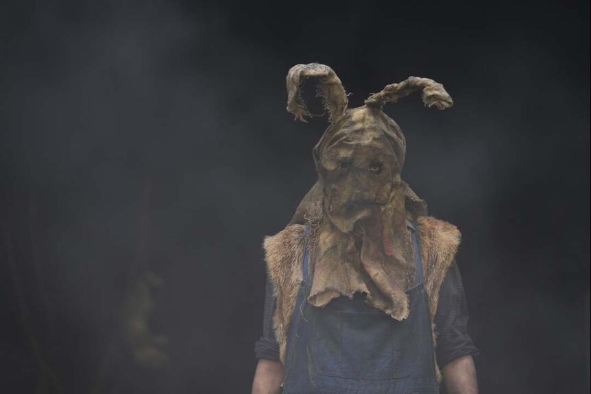 A man wears a "bunny ear" mask made of tattered fabric in John Carpenter's Suburban Screams 104