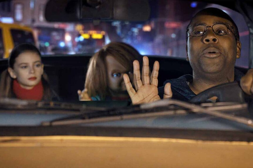Caroline Cross (Carina Battrick) and Chucky sit in the backseat of a cab and listen to the cab driver (Kenan Thompson) speak.