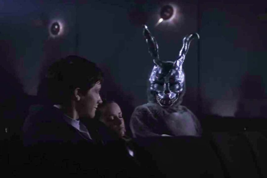 Donnie Darko (Jake Gyllenhaal) sits in a movie theater with a girl and looks at a scary anthromorphic rabbit Donnie Darko (2001).