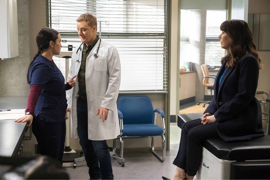 Asta Twelvetrees and Harry Vanderspeigle talk while a patient sits and watches in Resident Alien Episode 304.