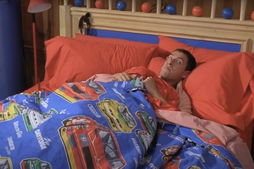 Billy Madison (Adam Sandler) pretends to sleep in his racecar themed sheets in Billy Madison (1995).