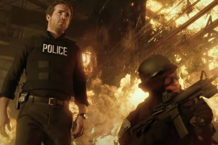 Nick Walker (Ryan Reynolds) walks through a burning building and past a man with a gun in R.I.P.D. (2013).