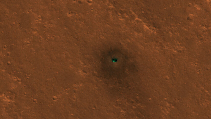 The Mars InSight lander seen from orbit by the Mars Reconnaissance Orbiter. The solar panels are visible as dark circles on either side of the lander itself. Credit: NASA/JPL/University of Arizona 