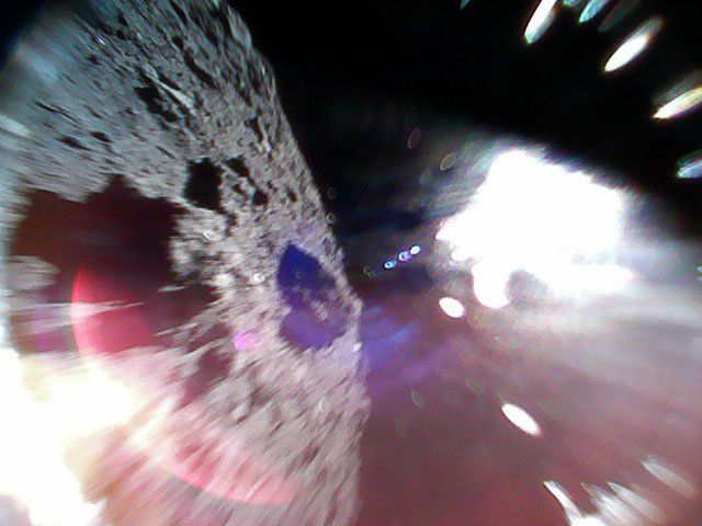 An image caught mid-bounce of the MINERVAII-1 A rover showing the surface of the asteroid Ryugu (left) and a reflection of sunlight (right). Credit: JAXA