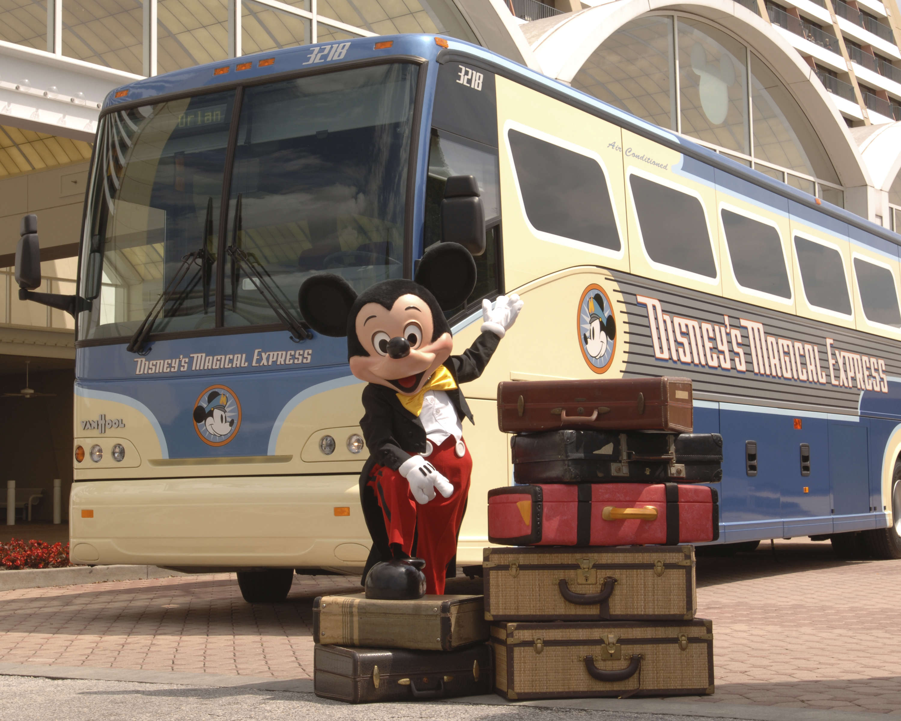 Mickey Mouse standing in front of Disney's Magical Express bus