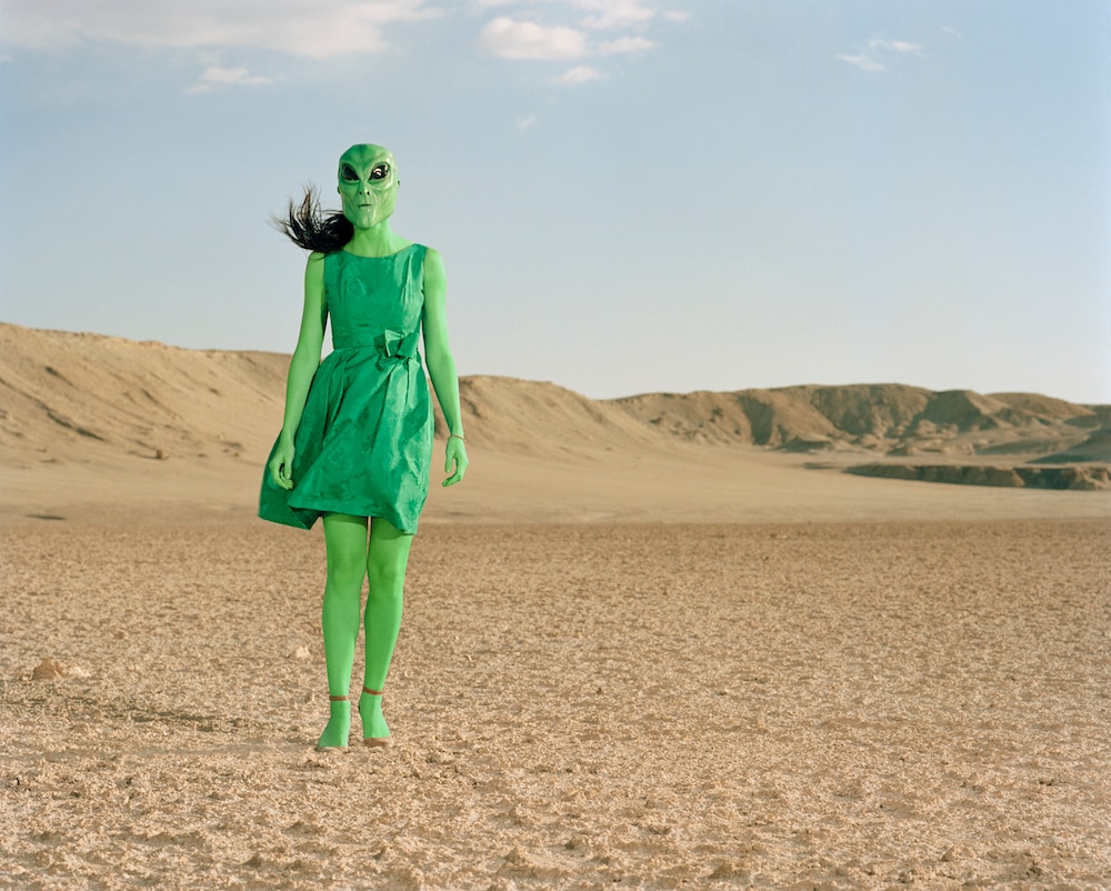 Extraterrestrial wearing green dress standing in desert.
