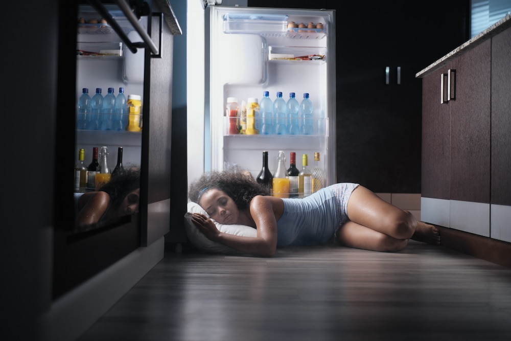 Young Woman Lying On Floor By Refrigerator At Home