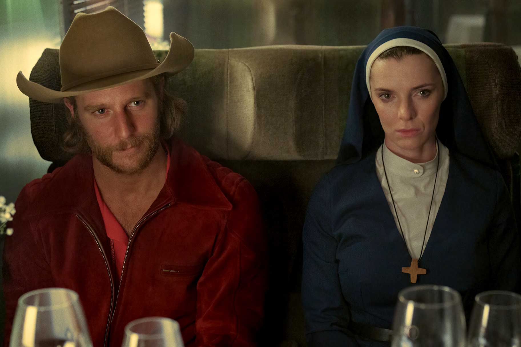 Jake McDorman as Wiley and Betty Gilpin as Simone sit next to each other with serious expressions on Mrs. Davis