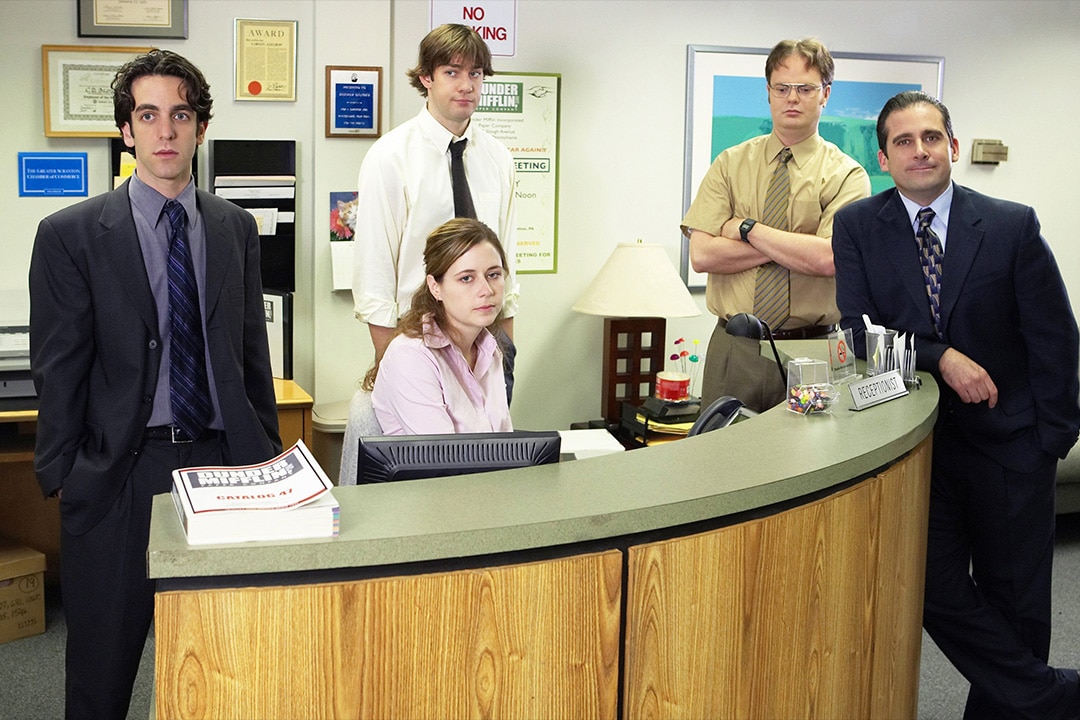 The cast of The Office Season 1 stands around a desk