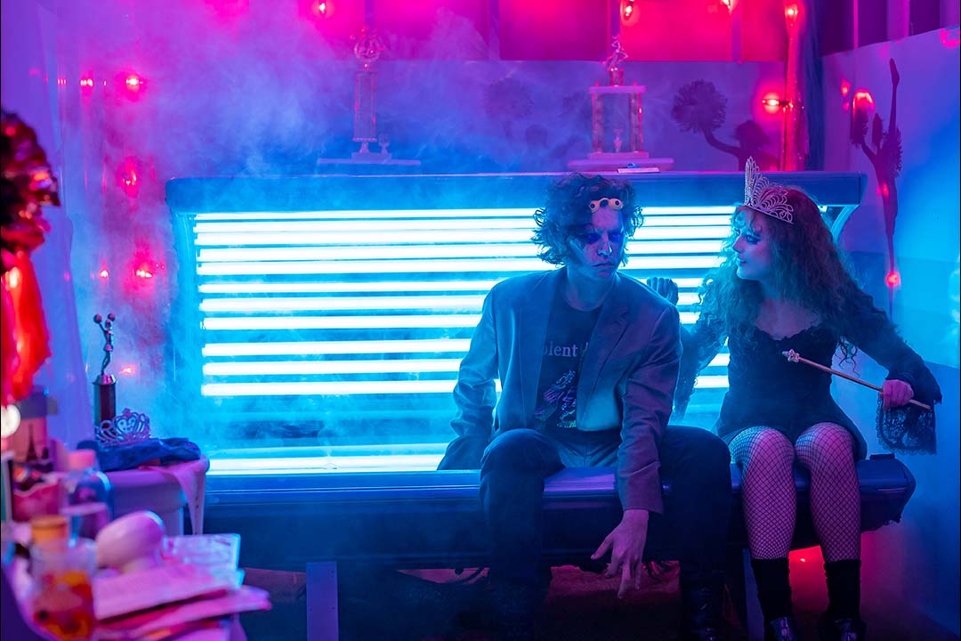 The Creature (Cole Sprouse) and Lisa Swallows (Kathryn Newton) sit together on the edge of a tanning bed in Lisa Frankenstein (2023).