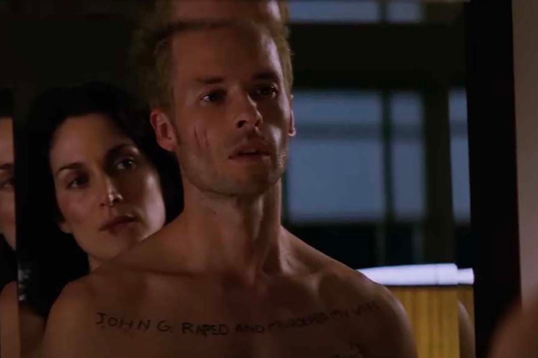Natalie (Carrie-Anne Moss) stands behind Leonard Shelby (Guy Pearce) in a mirror in Memento (2000).