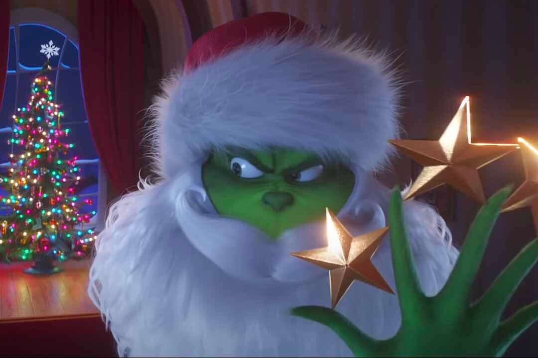 The Grinch (Benedict Cumberbatch) wears a Santa disguise and holds stars in between his finger with a Christmas tree in the background in The Grinch (2018).