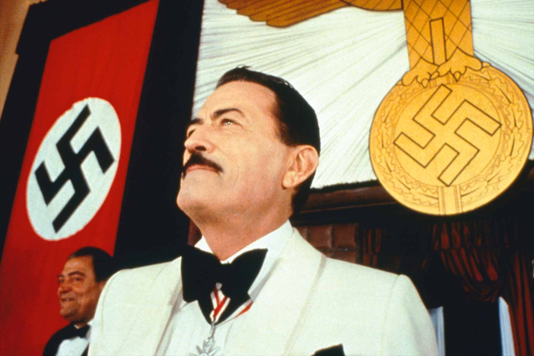 Dr. Josef Mengele (Gregory Peck) appears with the Nazi flag and decorations behind him in The Boys from Brazil (1978).