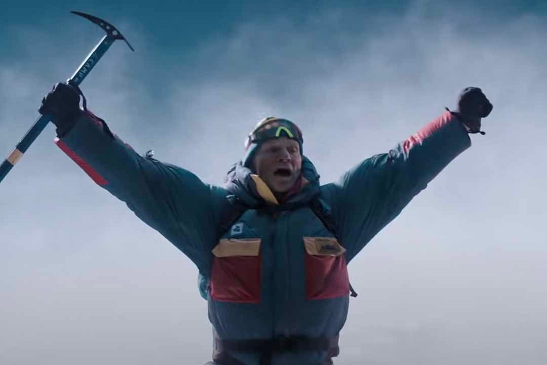 A bundled up mountain climber raises his arms with a pickaxe in one hand in Everest (2015).