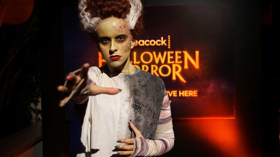 A scare actor dressed as the Bride of Frankenstein with their hand stretched out to the camera.