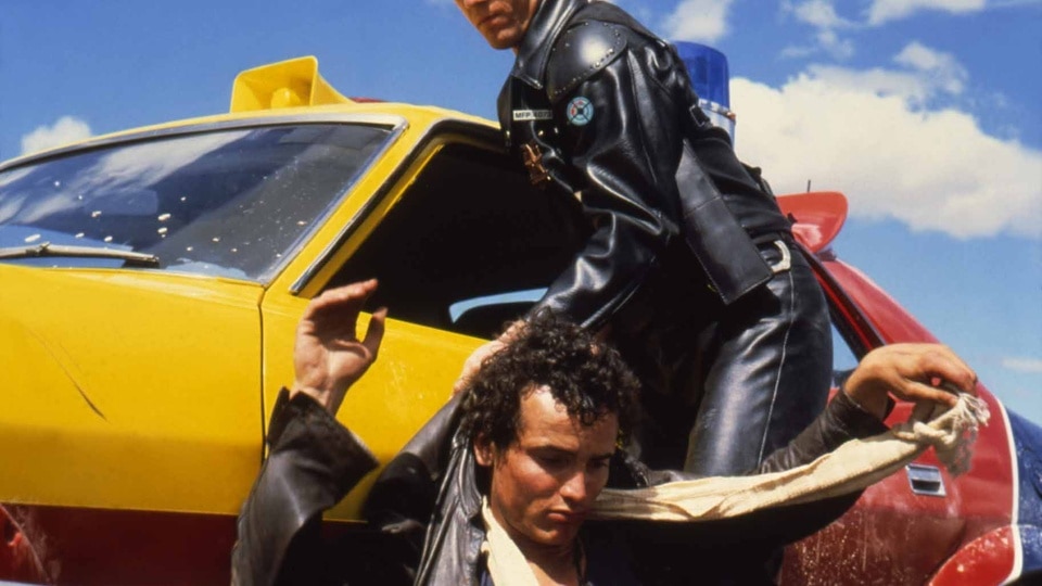 Max Rockatanksy (Mel Gibson) attacks a kneeling Toecutter (Hugh Keays-Byrne) in Mad Max (1979).