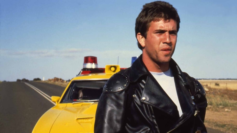 Max Rockatanksy (Mel Gibson) stands in front of a yellow car in Mad Max (1979).