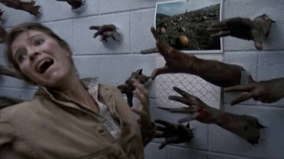 Zombie hands reach out of a wall toward Dr. Sarah Bowman (Lori Cardille) in Day of the Dead (1985).