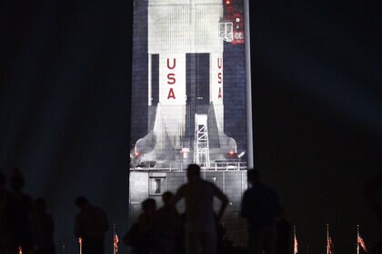 The Saturn V rocket projected at night against the Washington Monument