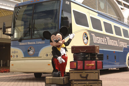 Mickey Mouse standing in front of Disney's Magical Express bus