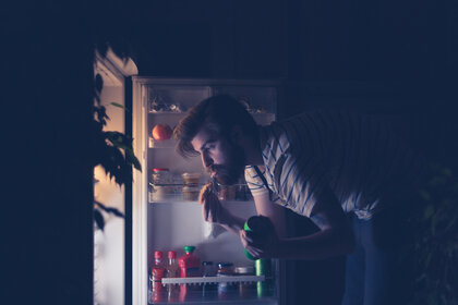 Man having snack in front of the refrigerator at night.