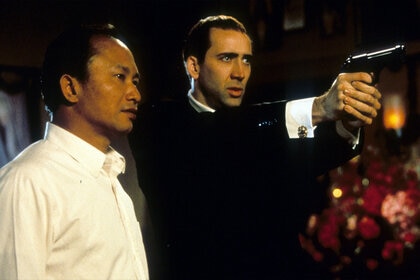 Director John Woo watches as Nicolas Cage aims pistol in between scenes from the film 'Face/Off' (1997)