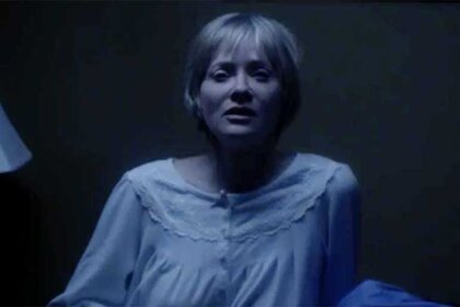 A woman sits up in bed at night in a nightgown in a scene from We Are Still Here