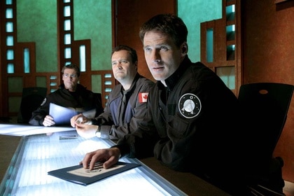 Michael Shanks, David Hewlett, and Ben Browder at a conference table in Stargate SG-1