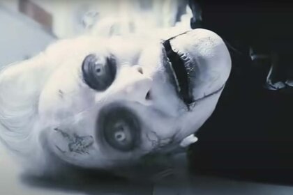 A puppet-like corpse with white skin and hair and black features.