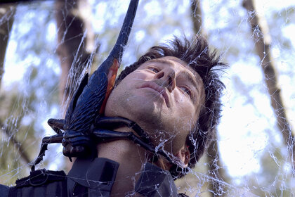 A distressed John Sheppard (Joe Flanigan) is entangled with a bug in its web in Stargate: Atlantis Season 1.