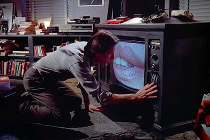 Max Renn (James Woods) examines a TV with lips on the screen in Videodrome (1983).