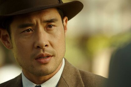 A close-up of Dr. Ben Song, who is wearing a hat, looking at another character while outdoors.