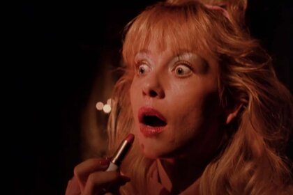 A blonde young woman about to apply lipstick appears shocked in Night of the Demons (1988).