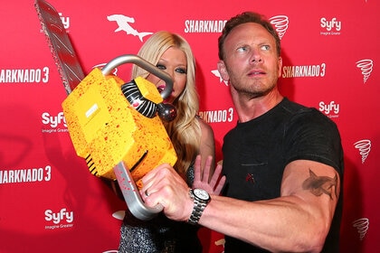 Tara Reid (L) and Ian Ziering hold a yellow chainsaw together on the red carpet.